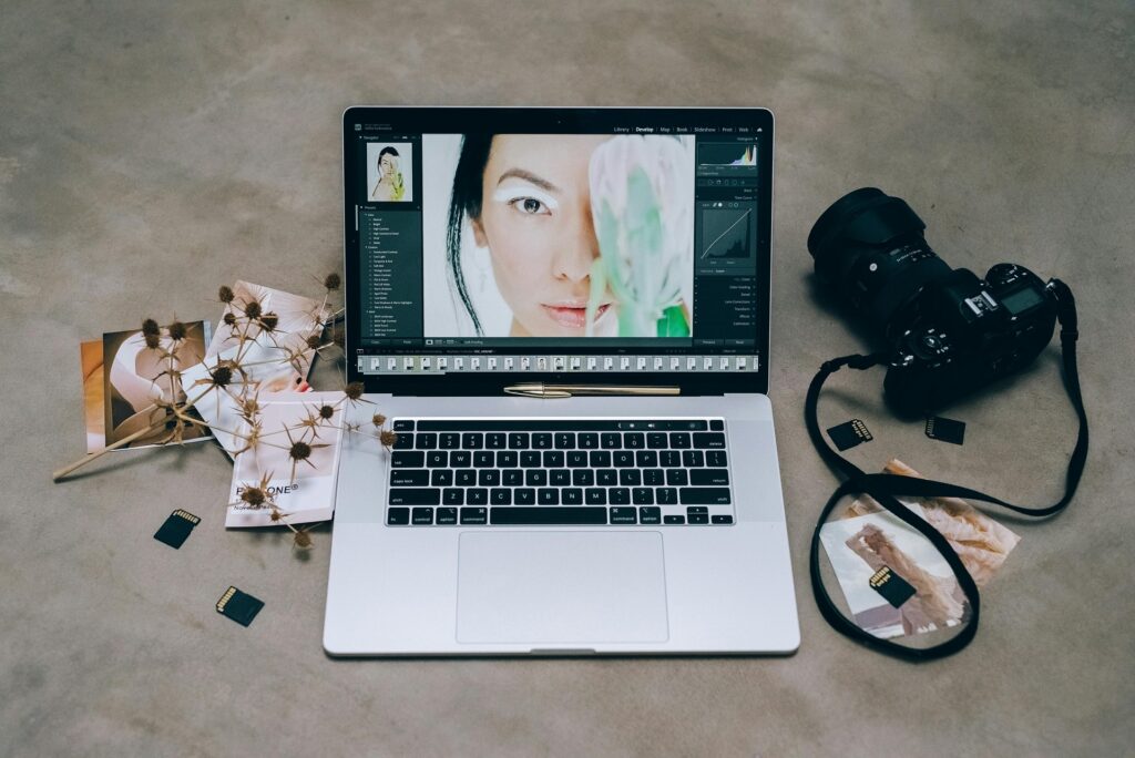 Computer with a photo that a photographer is editing and a camera and flowers in the background. 