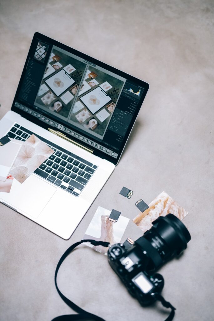 A picture of a laptop with a photo, a camera, sd cards, and pictures on a desk.