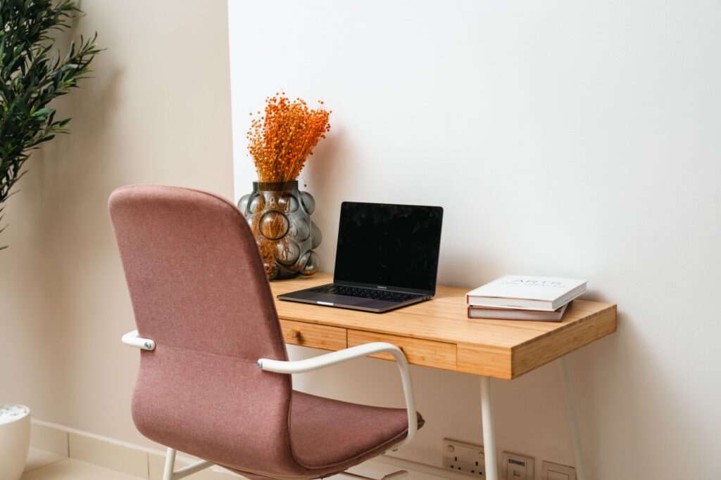 A pink chair at a desk with a computer and books sitting on top. 
