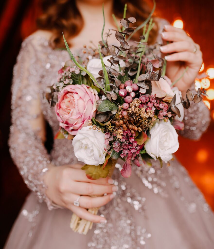 A bride in a wedding dress holding a bouquet of flowers of peonies, roses, berries, and greenery.